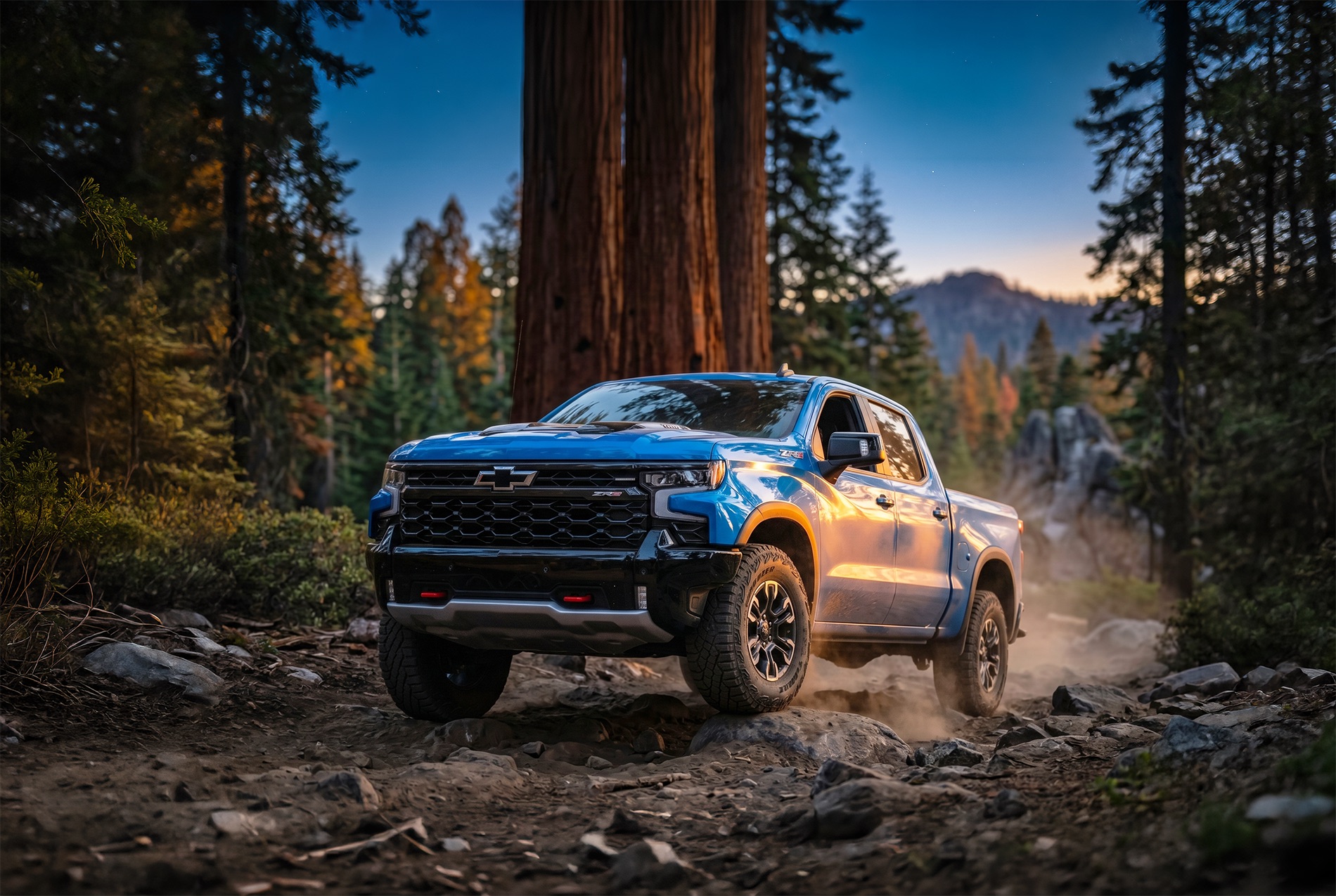 2026 Chevrolet Silverado 1500 ZR2 driving on a rocky trail through a thick forest with mountains at sunset