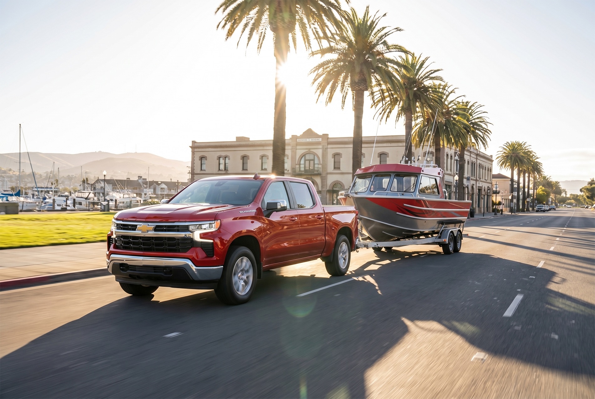 2026 Chevrolet Silverado 1500 towing a boat through a town along the ocean with a harbor in the distance