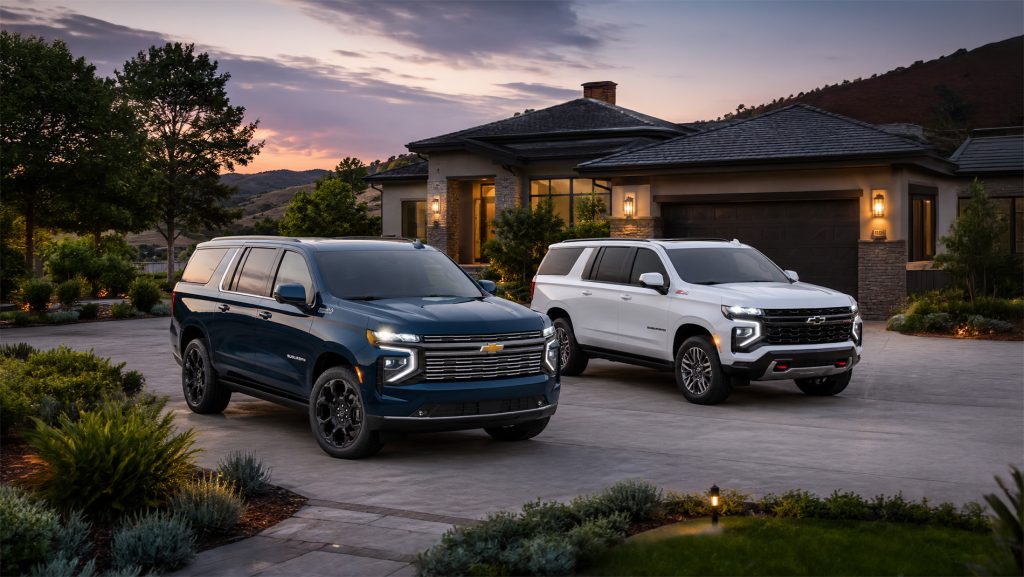 A blue and white 2026 Chevrolet Suburban parked side by side in a modern residential driveway at sunset, highlighting distinct styling between luxury and off‑road Z71 trims available at Delta Chevrolet in Pittsburg, CA.