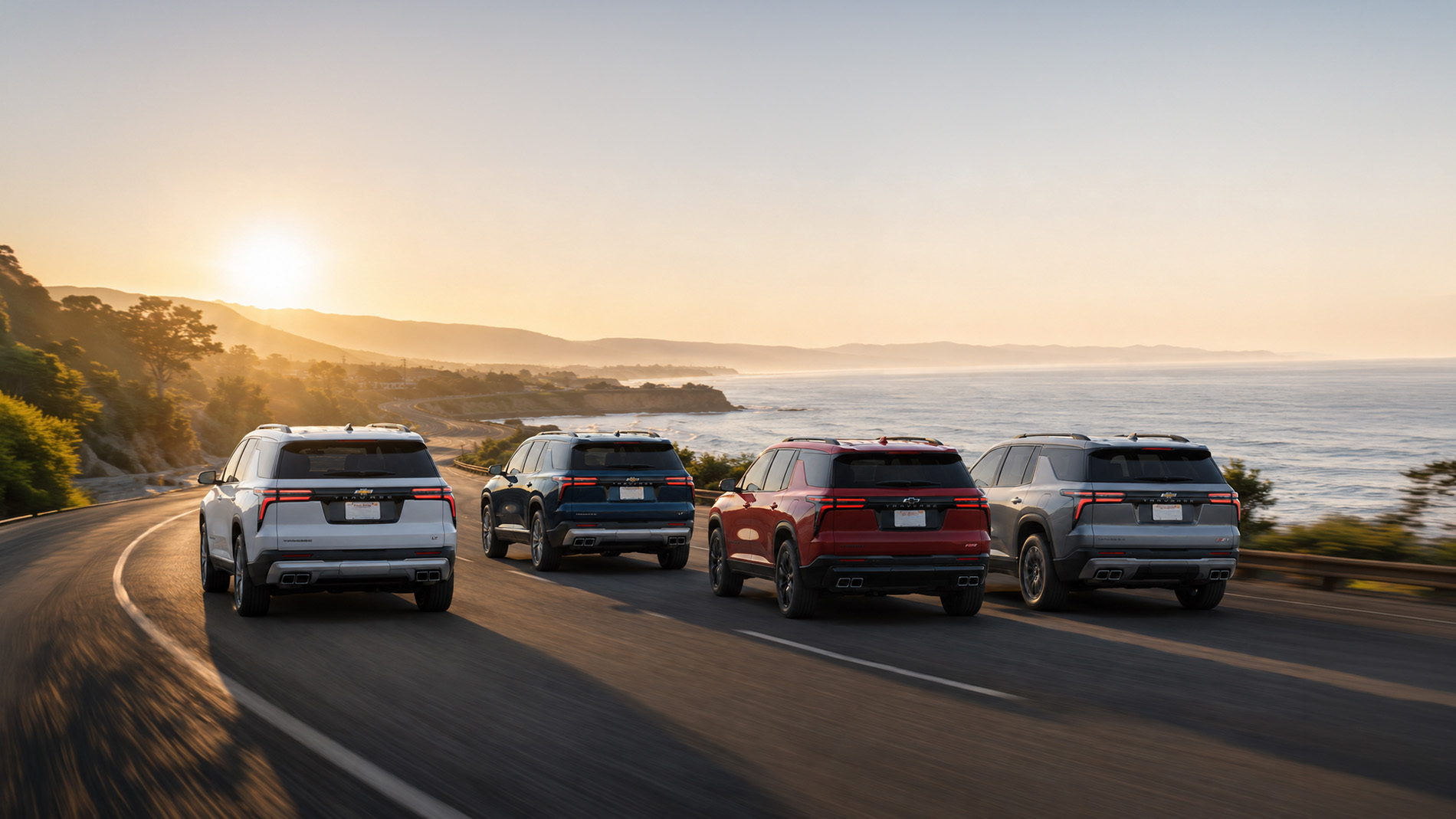 Four 2026 Chevrolet Traverse SUVs driving along a coastal highway at sunset, with the Pacific Ocean and rolling hills in the background, illustrating style and versatility across Traverse trim levels.
